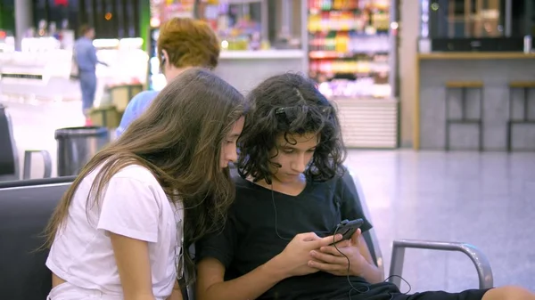 As crianças na área de espera do aeroporto usam um smartphone. conceito de viagem — Fotografia de Stock