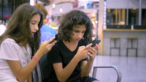 Los niños en la sala de espera del aeropuerto utilizan un teléfono inteligente. concepto de viaje — Foto de Stock