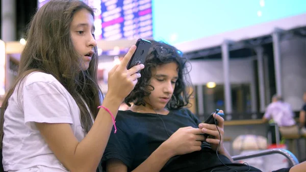 As crianças na área de espera do aeroporto usam um smartphone. conceito de viagem — Fotografia de Stock