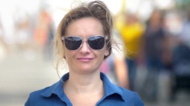 Gözlüklü güzel kadın, kameraya bakıyor, yakın çekim. sıcak yaz günü. Arka planda hareket halinde bulanık insanlar hareketli kalabalık.