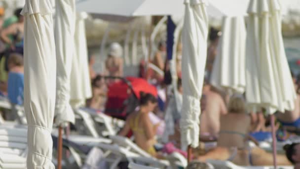 Niewyraźne tło. leżaki i parasole na plaży, nierozpoznawalnych ludzi odpoczynku — Wideo stockowe