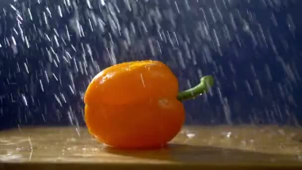 Sladký oranžový pepř na tmavém pozadí ve studiu pod tryskami deště. — Stock video