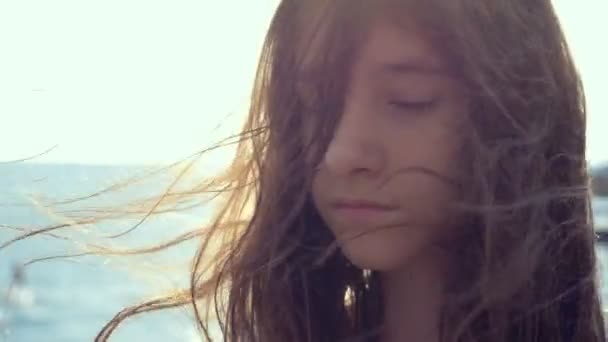 Tizenéves lány egy fehér ruhában, hosszú hajú néz elgondolkodva a tengerbe. szél alakul haj — Stock videók