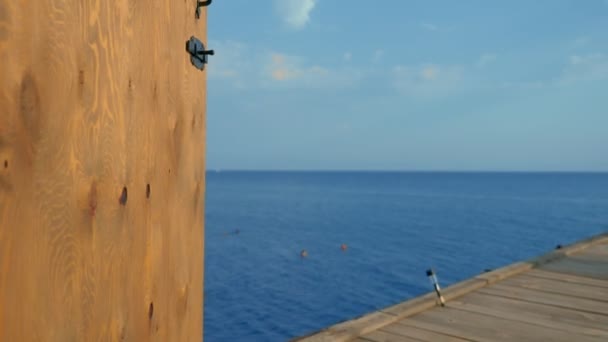 En dörr till lusthuset på piren ovanför havet, med en dekorativ spegel och havet och himlen reflekteras i den. — Stockvideo