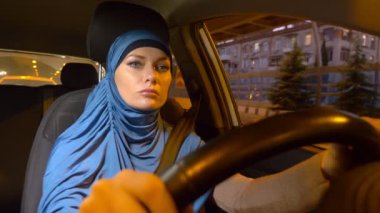 mavi bir hijab güzel Müslüman kadın şehrin sokaklarında akşam bir araba sürmek.