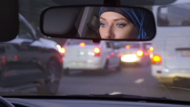 Odraz ženy v hidžábu ve zpětném zrcátku auta při jízdě v dopravní zácpě večer. Muslimská žena, která řídí auto. — Stock video