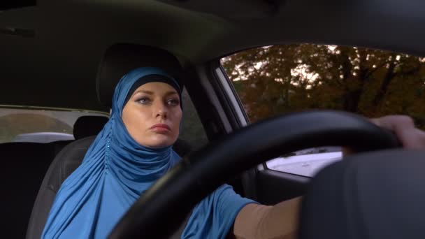 Όμορφη μουσουλμανική γυναίκα με μπλε μαντίλα οδηγώντας ένα αυτοκίνητο. βόλτες κατά τη διάρκεια της ημέρας στους δρόμους της πόλης. — Αρχείο Βίντεο
