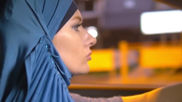 Mavi bir hijab güzel Müslüman kadın şehrin sokaklarında akşam bir araba sürmek. — Stok video