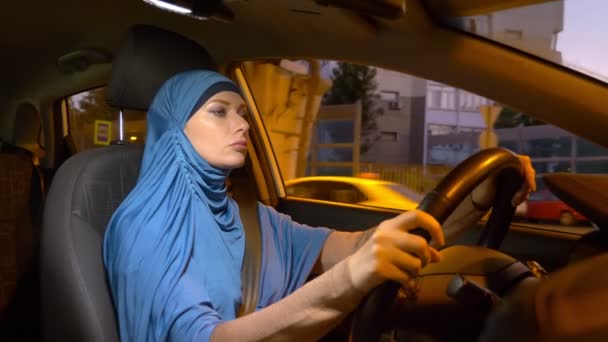 Belle femme musulmane dans un hijab bleu monte en voiture le soir dans les rues de la ville . — Video