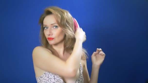Concepto de chica pin-up. Mujer pin-up endereza su cabello, mirando a la cámara, fondo azul. espacio de copia — Vídeos de Stock