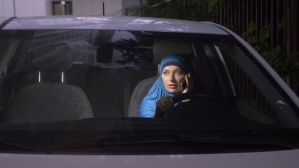 Vista através do pára-brisas de um carro. Mulher muçulmana em hijab azul falando ao telefone enquanto dirige um carro . — Vídeo de Stock