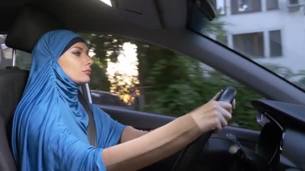 Mooie moslim vrouw in blauwe hijab rijden een auto. ritten overdag op de straten van de stad. — Stockvideo