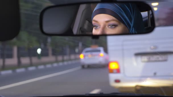 Odraz ženy v hidžábu ve zpětném zrcátku auta při jízdě v dopravní zácpě večer. Muslimská žena, která řídí auto. — Stock video