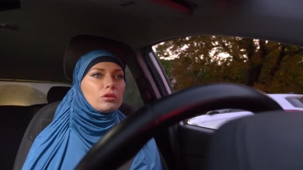 Schöne muslimische Frau im blauen Hidschab am Steuer eines Autos. Fahrgeschäfte tagsüber auf den Straßen der Stadt. — Stockvideo