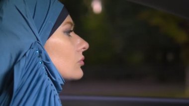 mavi bir hijab güzel Müslüman kadın şehrin sokaklarında akşam bir araba sürmek.