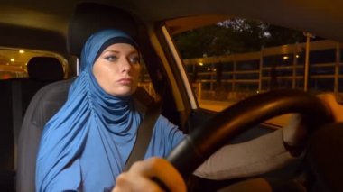 mavi bir hijab güzel Müslüman kadın şehrin sokaklarında akşam bir araba sürmek.
