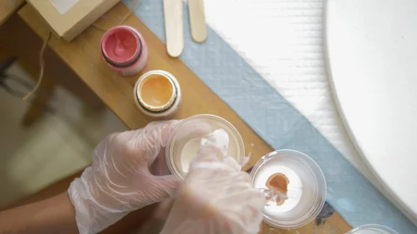 Primer plano, mezclando pintura en una taza desechable. artistas lugar de trabajo. preparación del flujo de trabajo para trabajar con pinturas acrílicas sobre lienzo. arte fluido — Foto de Stock