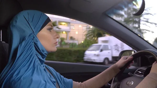 Hermosa mujer musulmana en hiyab azul conduciendo un coche. paseos durante el día por las calles de la ciudad . — Foto de Stock
