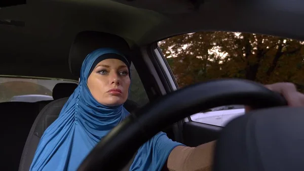 beautiful muslim woman in blue hijab driving a car. rides during the day on the streets of the city.