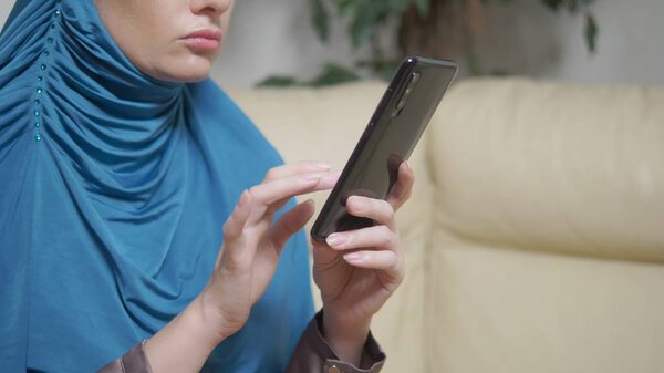 beautiful muslim woman in blue hijab using a mobile phone sitting on a sofa