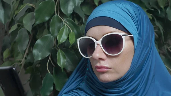 Portrait of a beautiful muslim caucasian woman wearing sunglasses on a background of ficus foliage — Stock Photo, Image