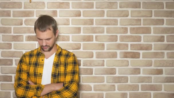 Upset handsome man in a fashionably yellow checkered shirt against a brick wall, copy space. gestures and emotions concept — Stock Video