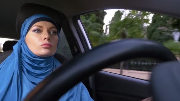 Όμορφη μουσουλμανική γυναίκα με μπλε μαντίλα οδηγώντας ένα αυτοκίνητο. βόλτες κατά τη διάρκεια της ημέρας στους δρόμους της πόλης. — Αρχείο Βίντεο