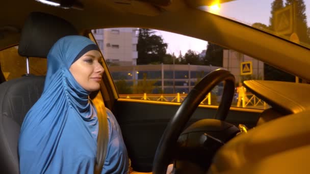 Belle femme musulmane dans un hijab bleu monte en voiture le soir dans les rues de la ville . — Video