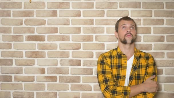 Sconvolto bell'uomo in una camicia a scacchi giallo alla moda contro un muro di mattoni, spazio copia. gesti ed emozioni concetto — Video Stock