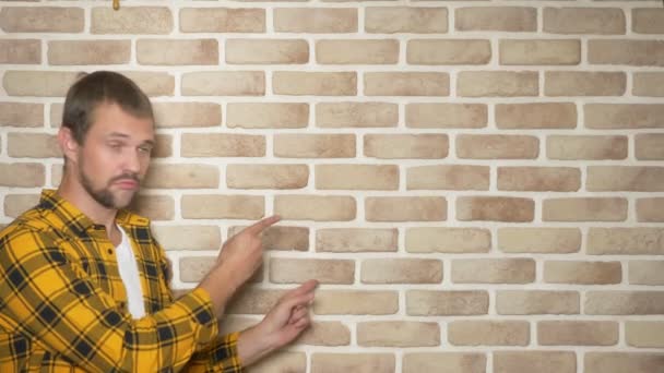 Joven guapo con una camisa amarilla a cuadros, apuntando a un lugar para el texto, un lugar para la publicidad — Vídeos de Stock