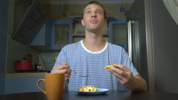 Мрійливий чоловік їсть їжу, сидячи на кухні вдома — стокове відео