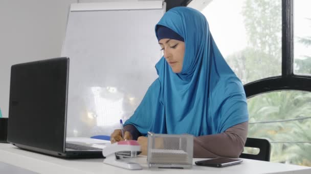 Красивая сауди бизнес-женщина в хиджабе работает в офисе с помощью ноутбука и смартфона, копировать пространство — стоковое видео