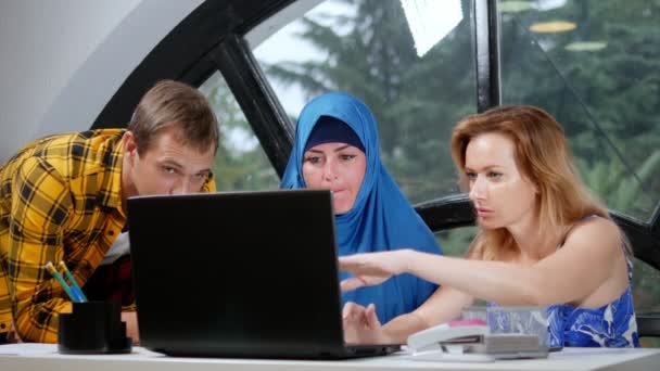 Conceito de equipa multinacional. mulher muçulmana em hijab, mulher caucasiana e homem caucasiano trabalhando juntos no escritório usando laptop . — Vídeo de Stock