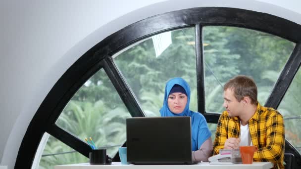 Concetto di squadra multinazionale. donna musulmana in hijab e uomo caucasico che lavorano insieme in ufficio utilizzando il computer portatile . — Video Stock