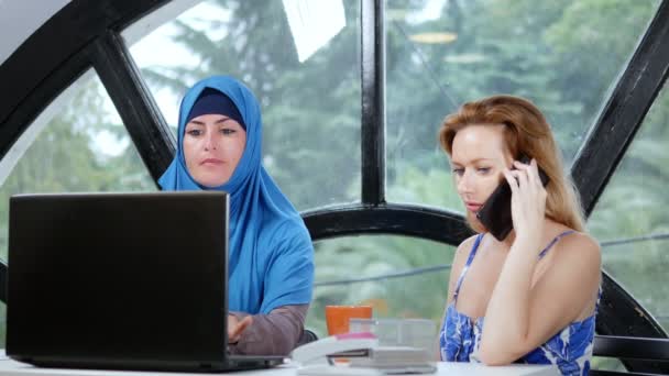 Wielonarodowej koncepcji zespołu. Dwie kobiety, muzułmańska kobieta w hidżab i kaukaski kobieta w otwartym szczycie, współpracują ze sobą w biurze przy użyciu laptopa. — Wideo stockowe