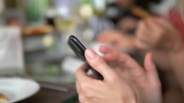 Bir aile veya dost akşam yemeği sırasında bir restoranda bir akıllı telefon gadget kullanarak bir mobil akıllı telefon ile Kadın eller.