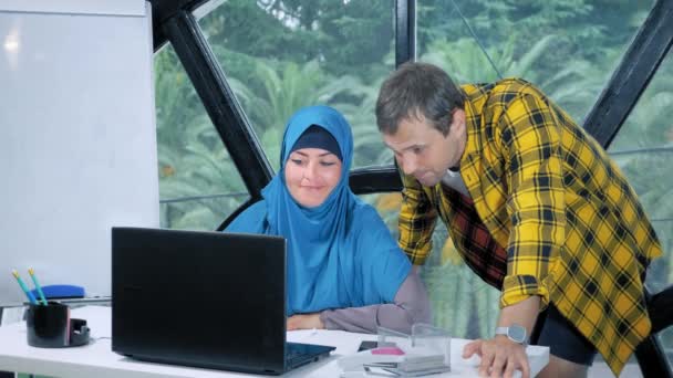 Многонациональная командная концепция. Мусульманка в хиджабе и кавказский мужчина работают вместе в офисе с помощью ноутбука . — стоковое видео