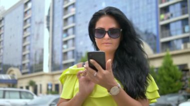 Şehir merkezinde yürüyen güzel genç esmer kadın akıllı telefon kullanır. güneşli yaz günü. başarılı bir yaşam tarzı. Kadın portresi