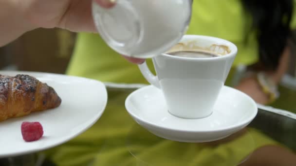 Krásná brunetka s dlouhými vlasy, které sedí při snídani ve venkovní kavárně, pije kávu s croissantem a odpočívá — Stock video