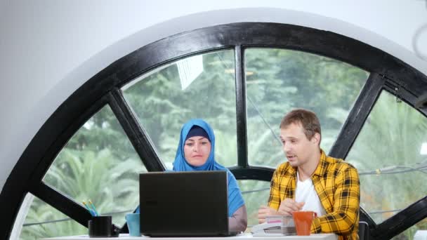 Многонациональная командная концепция. Мусульманка в хиджабе и кавказский мужчина работают вместе в офисе с помощью ноутбука . — стоковое видео