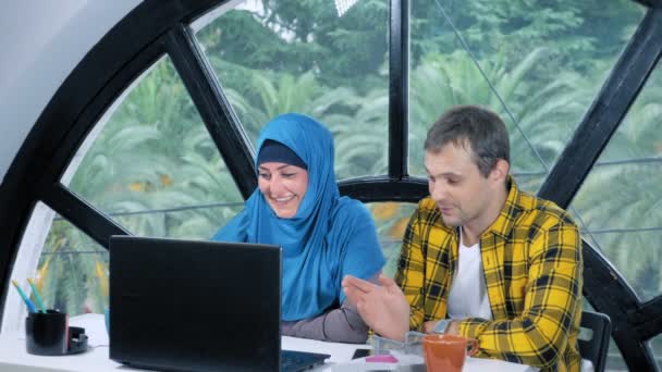 Wielonarodowej koncepcji zespołu. muzułmańska kobieta w hidżab i kaukaski mężczyzna pracujący razem w biurze za pomocą laptopa. — Wideo stockowe