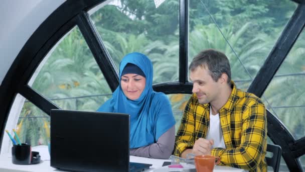 Concetto di squadra multinazionale. donna musulmana in hijab e uomo caucasico che lavorano insieme in ufficio utilizzando il computer portatile . — Video Stock