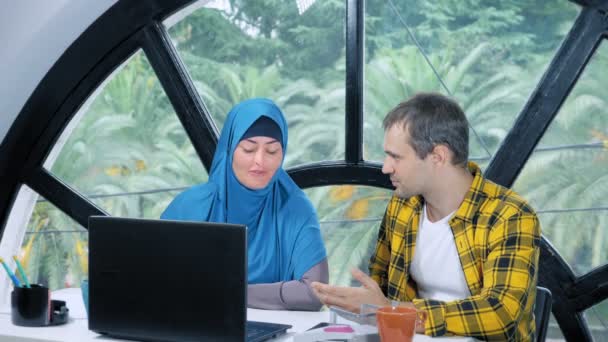 Concetto di squadra multinazionale. donna musulmana in hijab e uomo caucasico che lavorano insieme in ufficio utilizzando il computer portatile . — Video Stock