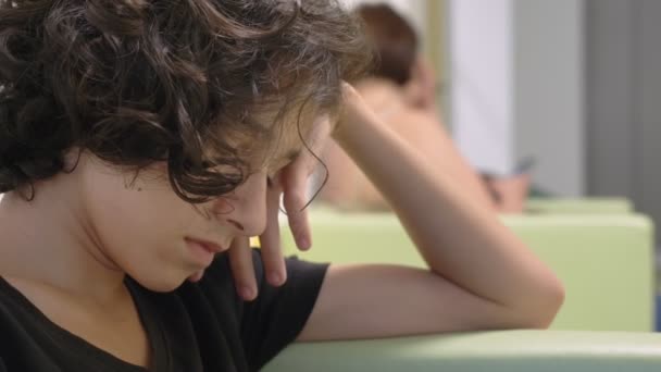 Teenager boy sitting in the lobby of a childrens clinic, waiting for a meeting with a doctor , using a smartphone. The concept of medical examination, health monitoring, preventive examination of — Stock Video