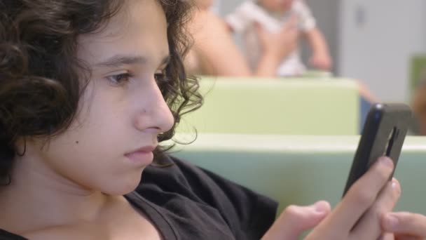 Teenager-Junge, der in der Lobby einer Kinderklinik sitzt und mit einem Smartphone auf einen Arzttermin wartet. das Konzept der ärztlichen Untersuchung, Gesundheitsüberwachung, Vorsorgeuntersuchung — Stockvideo