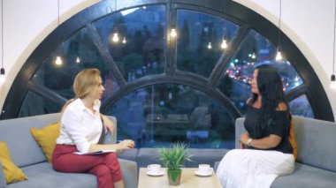 iki kadın kanepede oturan bir ofis boş alanda konuşan, çok uluslu iş kadınları kahve içme ve sohbet