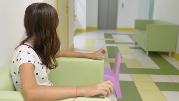 La niña está sentada en el vestíbulo de la clínica infantil, esperando una cita con el médico. concepto de examen médico, seguimiento de la salud, examen preventivo de los médicos . — Vídeos de Stock