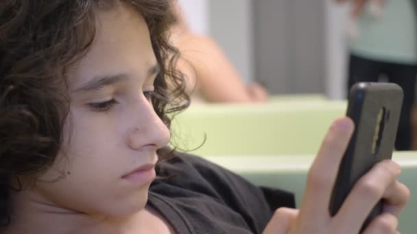 Adolescente sentado no átrio de uma clínica infantil, esperando uma reunião com um médico, usando um smartphone. O conceito de exame médico, monitoramento de saúde, exame preventivo de — Vídeo de Stock