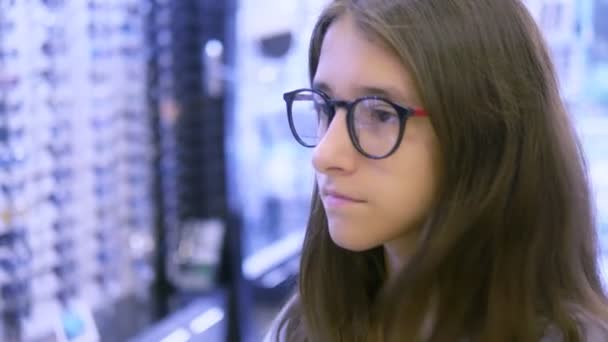 Auswahl von Fassungen für Brillen in Optik. Mutter und Tochter im Teenageralter wählen Brillengestell, während sie in einen großen Spiegel in Optik schauen. — Stockvideo
