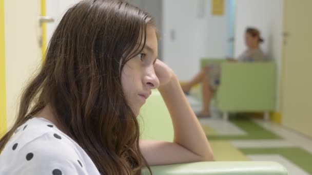 La niña está sentada en el vestíbulo de la clínica infantil, esperando una cita con el médico. concepto de examen médico, seguimiento de la salud, examen preventivo de los médicos . — Vídeos de Stock